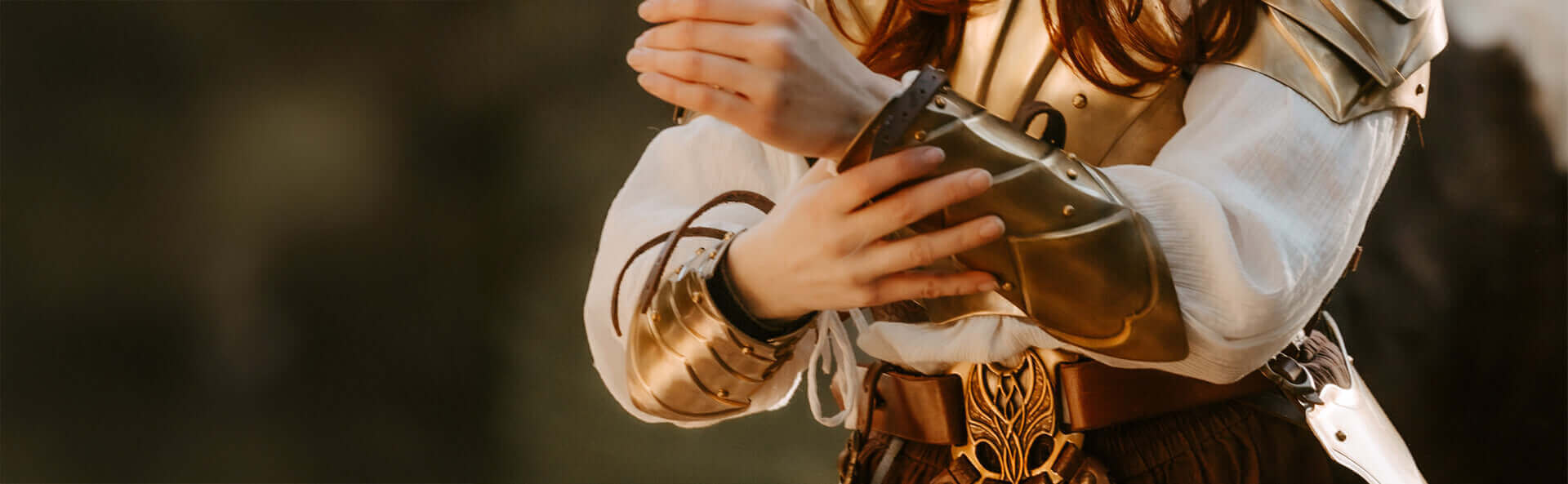Person in ornate armor holding a helmet against a blurred background