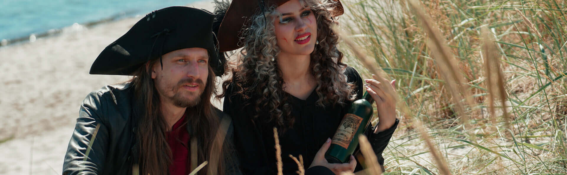 Two people in pirate costumes on a beach with grass and water in the background