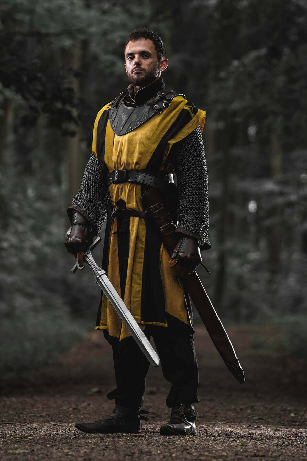 Person in medieval armor holding two swords in a forest setting