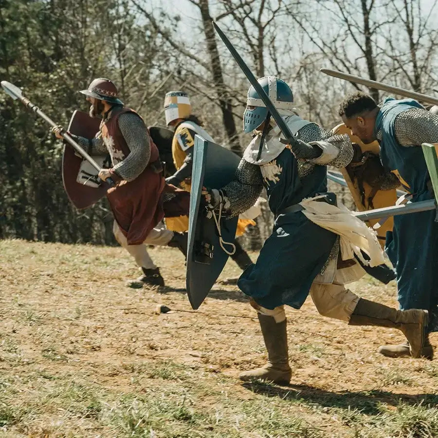 Group of armored warriors charging on a battlefield with shields and spears, showcasing medieval combat during a reenactment.