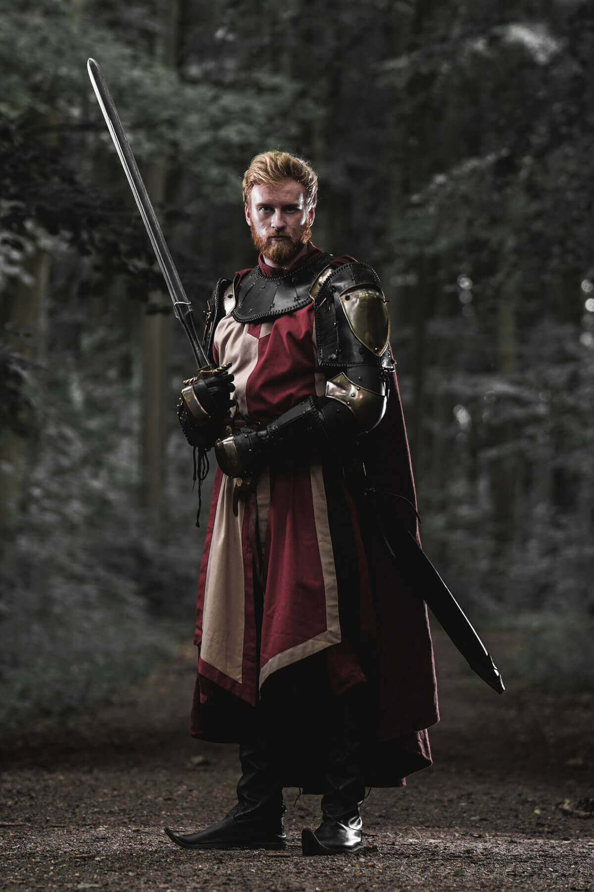 Man in medieval armor holding a sword in a forest setting